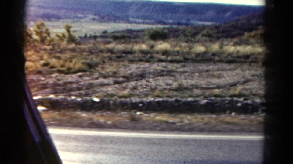 1967 Colorado passenger-side view showing a road edge, stony ground, shrubs, grasses, and distant terrain.