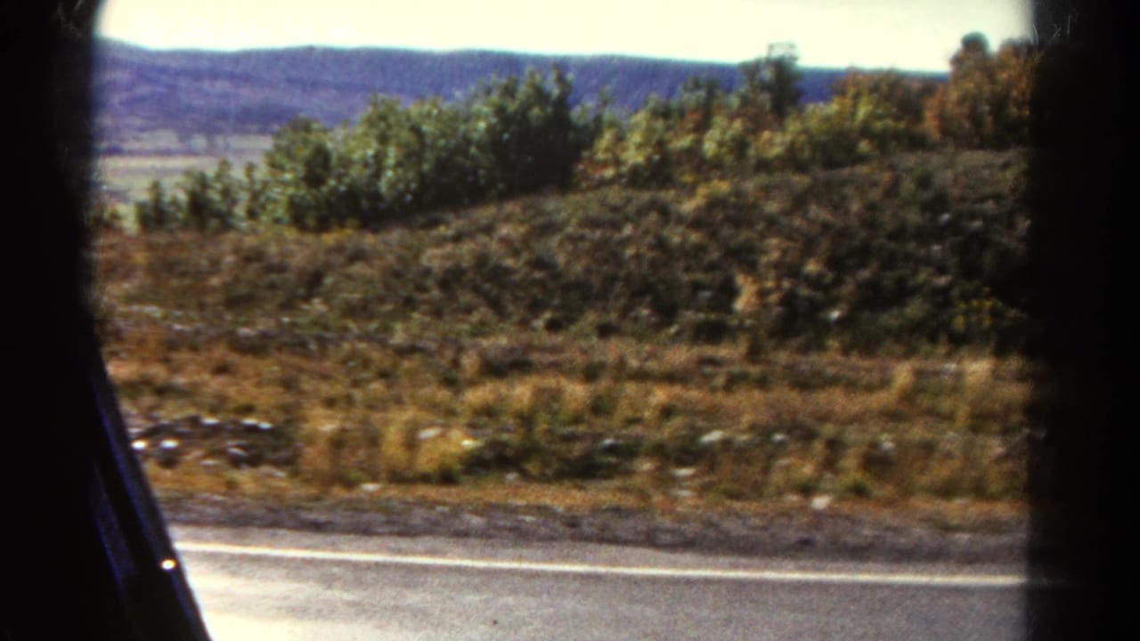1967 Colorado roadside landscape seen from a moving vehicle, with shrubs, dry grass, and a low ridge beyond the highway.
