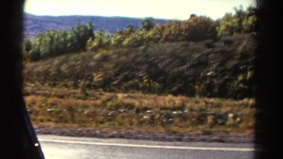 1967 Colorado home-movie view of a rocky roadside slope and brush, blurred by motion from the moving car.
