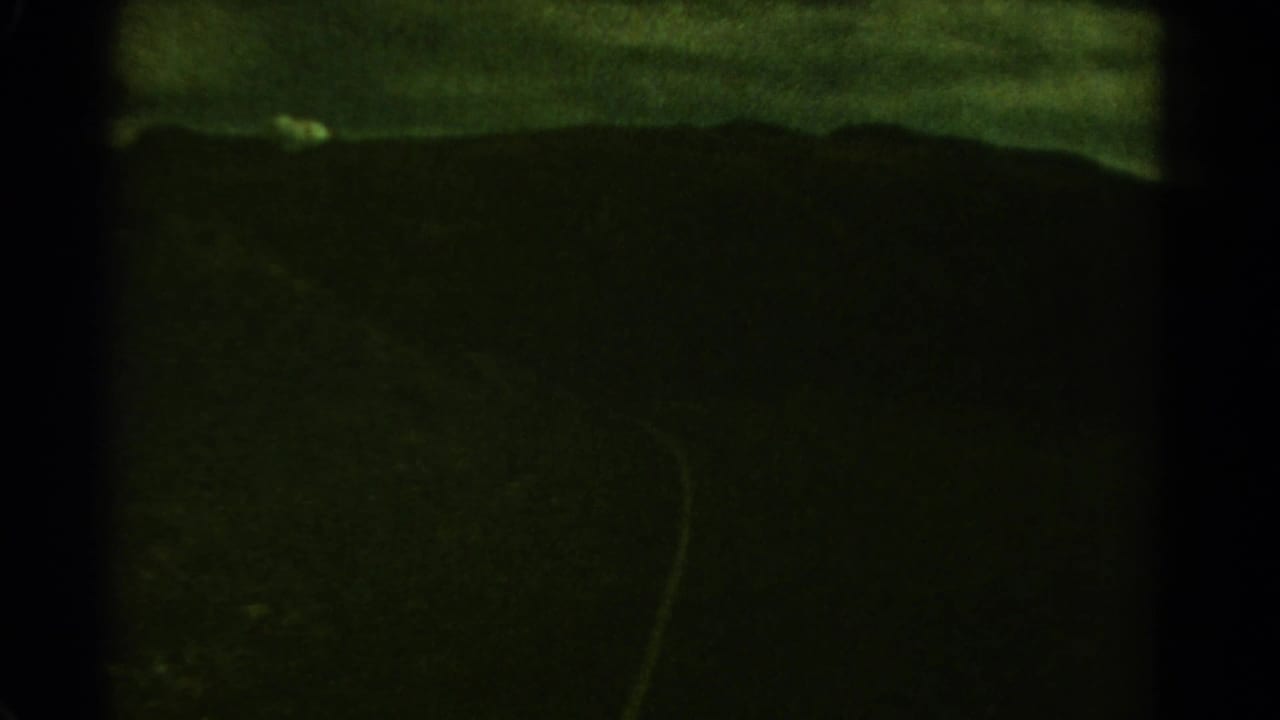 1967 Colorado 8mm frame showing distant mountain ridges beneath a green stormy sky, with heavy film grain and dark gate edges.