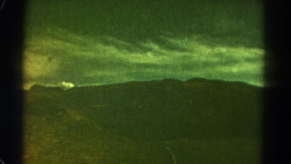 Aged 8mm Colorado travel frame showing storm clouds over mountain ridges, with grassy foreground and a faint curving road line.