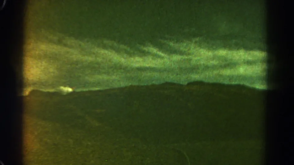 1967 8mm Colorado landscape frame with soft focus, green color shift, distant ridge, cloud cover, and a faint white shape near the horizon.