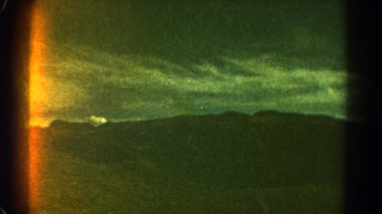 Green-tinted storm clouds over a dark mountain ridge with a bright light leak at the left edge.