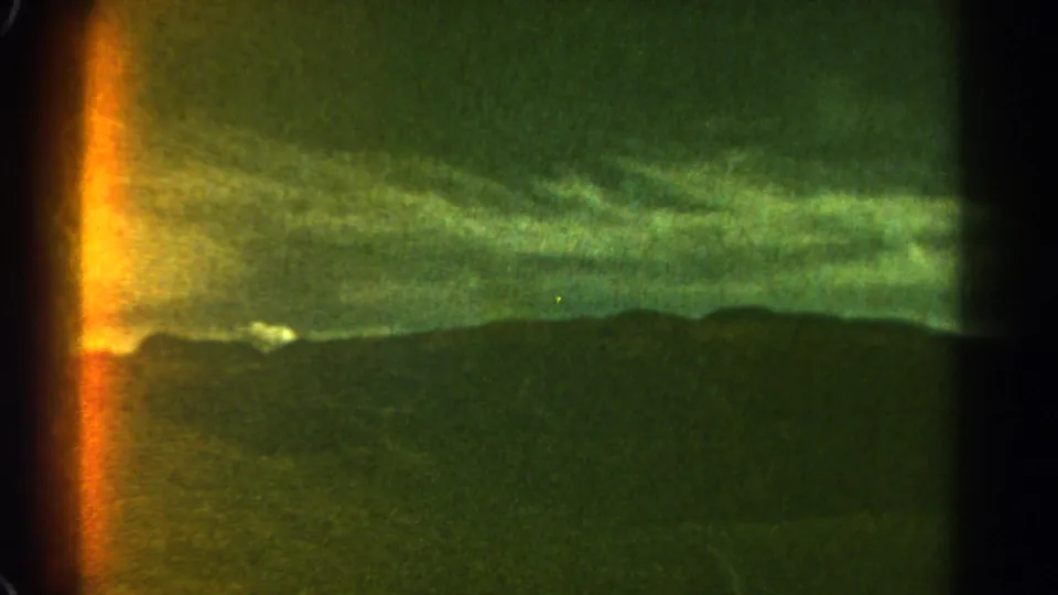1967 Colorado 8mm frame showing storm clouds above a dark mountain ridge, with visible grain and a bright orange light leak at the left edge.