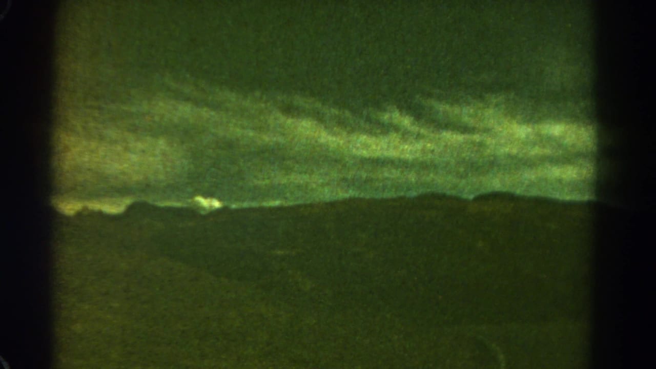 Dark ridge beneath layered green storm clouds, divided by a vertical film-frame bar.