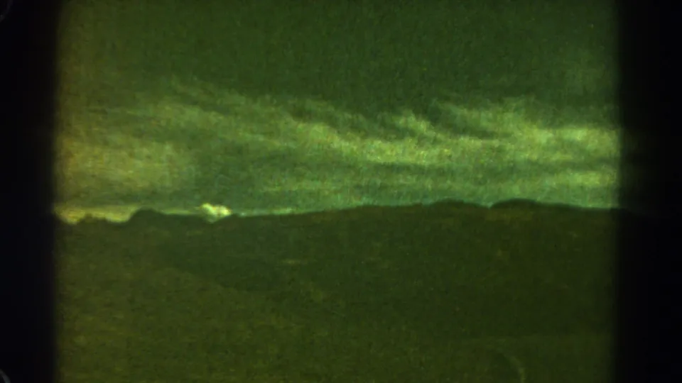 1967 Colorado 8mm frame with layered storm clouds over a mountain ridge, softened by grain and a central dark film-frame division.