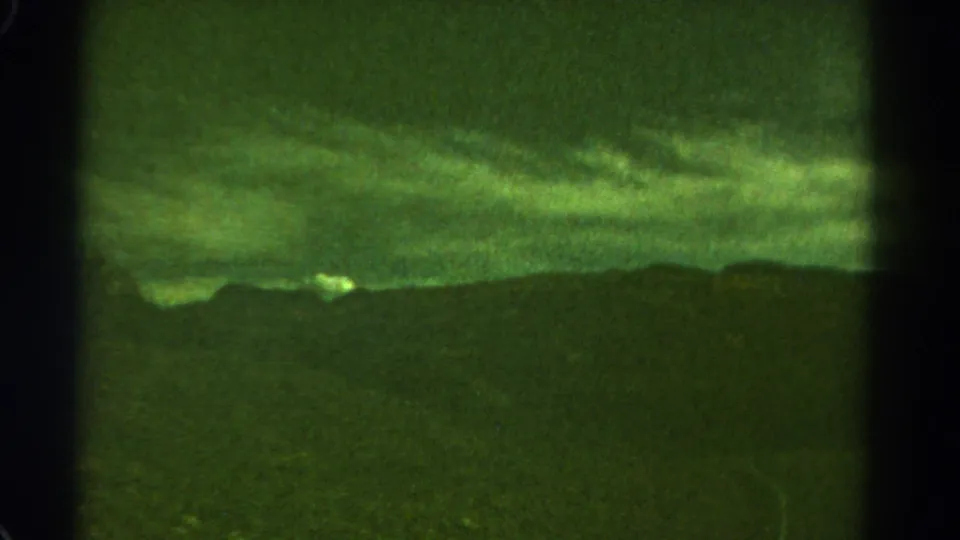 1967 Colorado 8mm frame showing a dark mountain ridge below a greenish storm sky, with soft focus, grain, and visible frame borders.