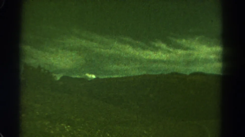 1967 Colorado 8mm frame showing low storm clouds above a dark ridge, with rocky foreground texture and pronounced archival grain.