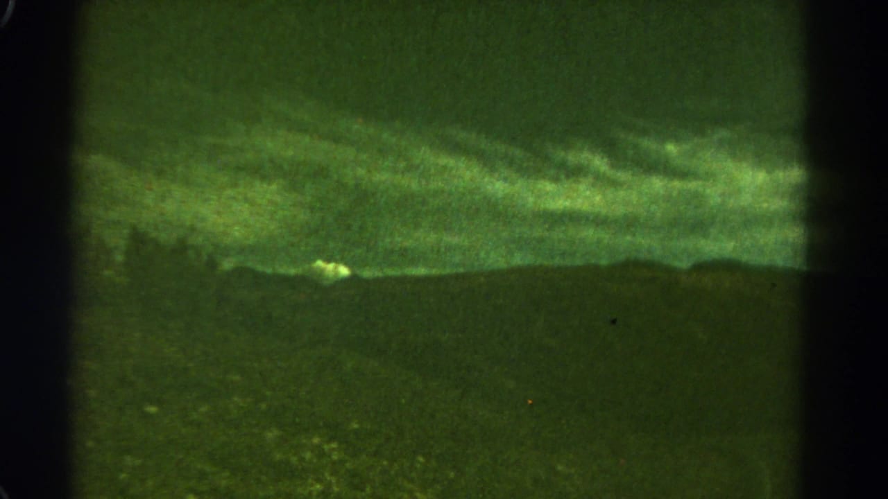 Green-tinted dark mountain silhouette beneath a cloudy sky with film gate edges.