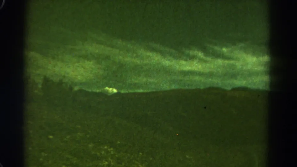 1967 Colorado 8mm frame showing a green-tinted mountain silhouette under a cloudy sky, with visible film grain and gate edges.