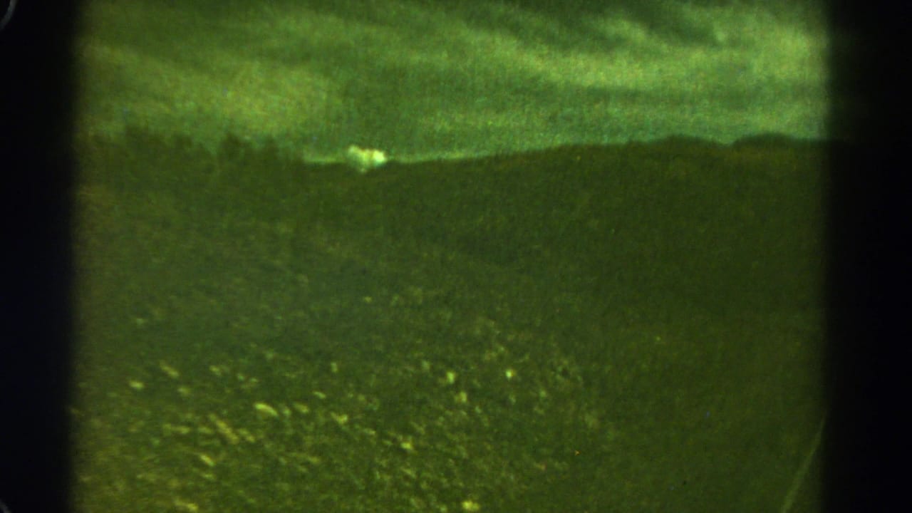 Dark green landscape and distant ridge under a cloudy sky with vertical film edge shadows.
