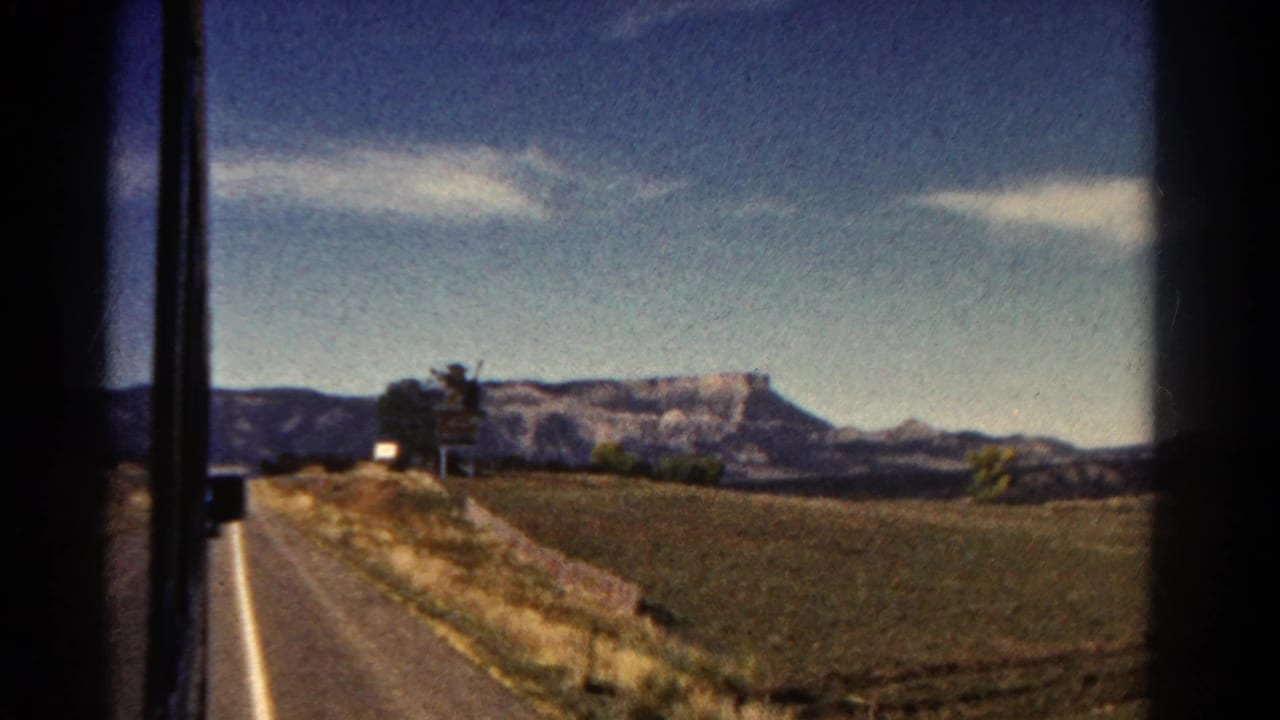 Distant mesa and fields viewed past dark window edges from a moving vehicle or train.