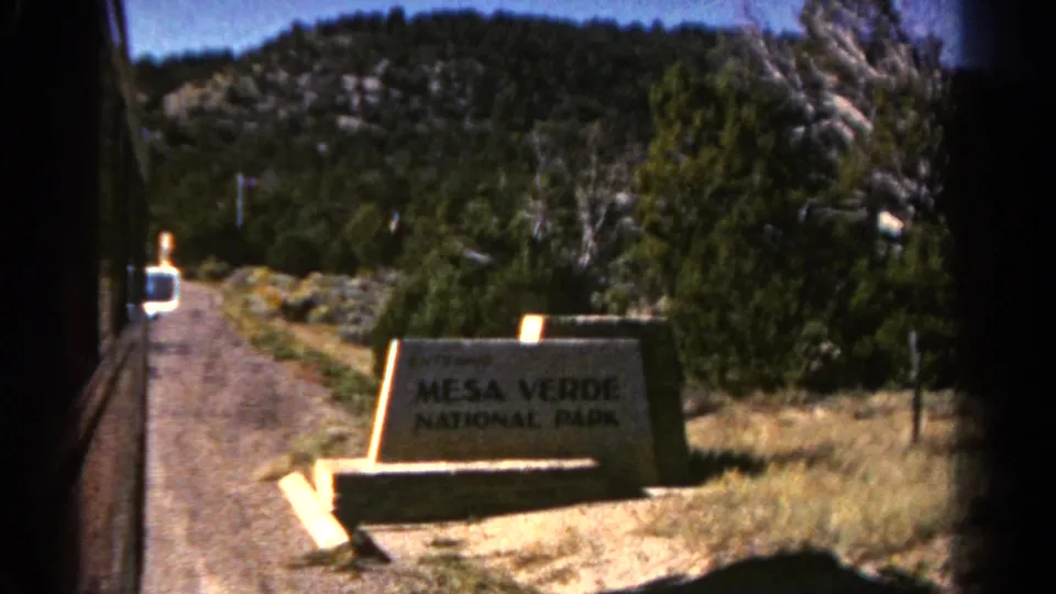 1967 8mm view of the Mesa Verde National Park entrance sign along a gravel roadside in Colorado.