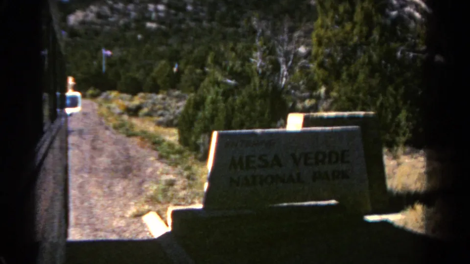 The 1967 home-movie camera passes the Mesa Verde National Park sign from a vehicle on the roadside.