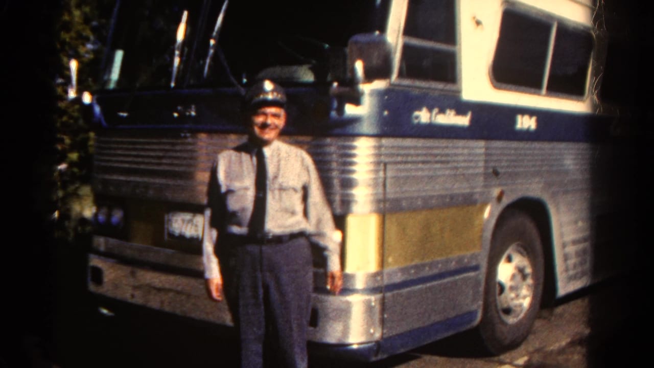 A uniformed adult man stands in sunlight beside a large ribbed metal motorcoach marked with the number 104.
