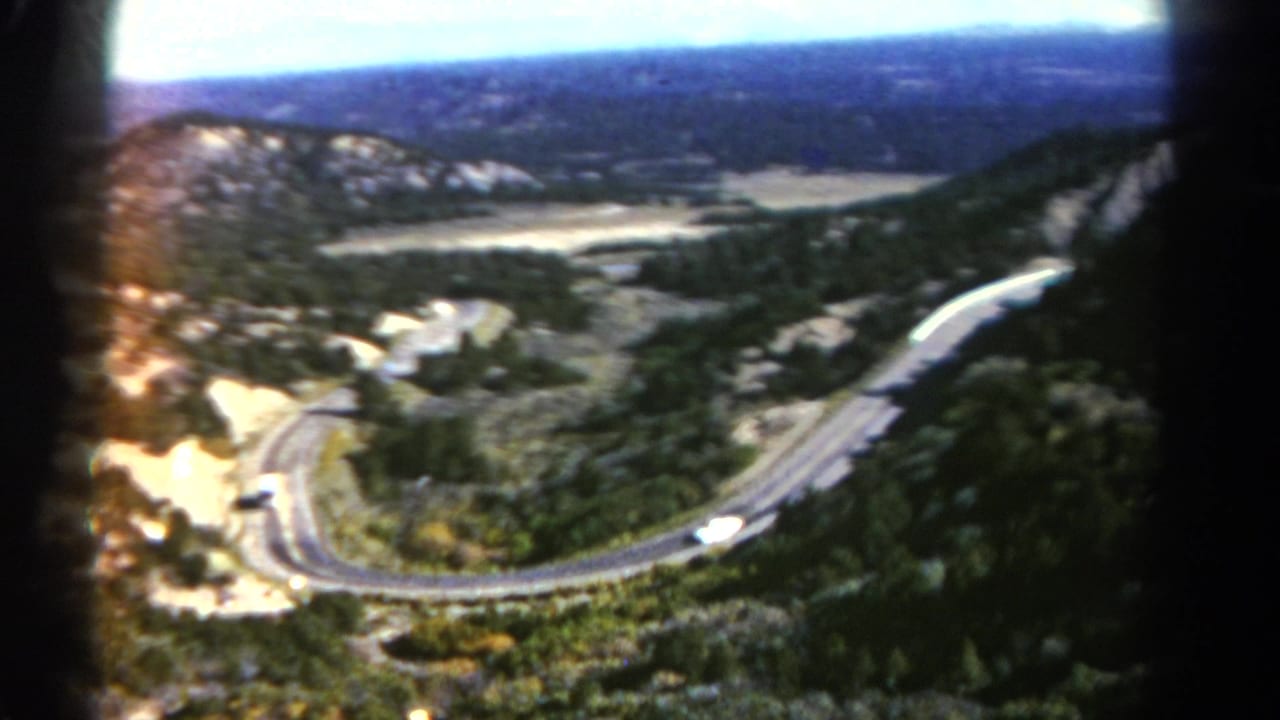 Winding paved mountain highway seen from above with small vehicles on the curves.