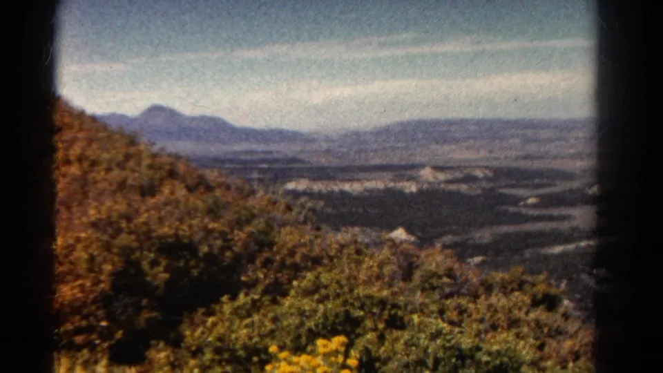 1967 Colorado 8mm frame showing hillside brush and yellow flowers in front of a broad valley with low mountains on the horizon.