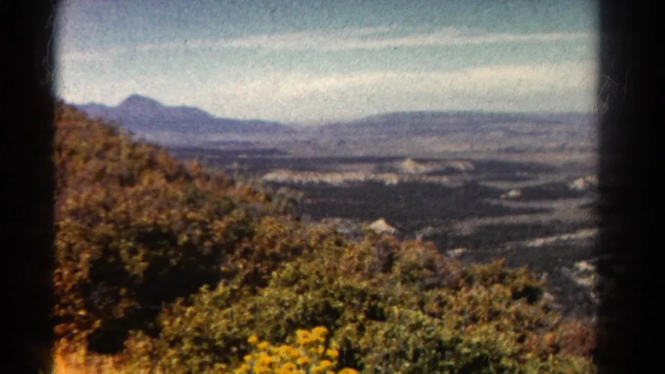 1967 Colorado 8mm frame looking from a hillside over foliage, a broad valley, winding water, and hazy mountain ridges.