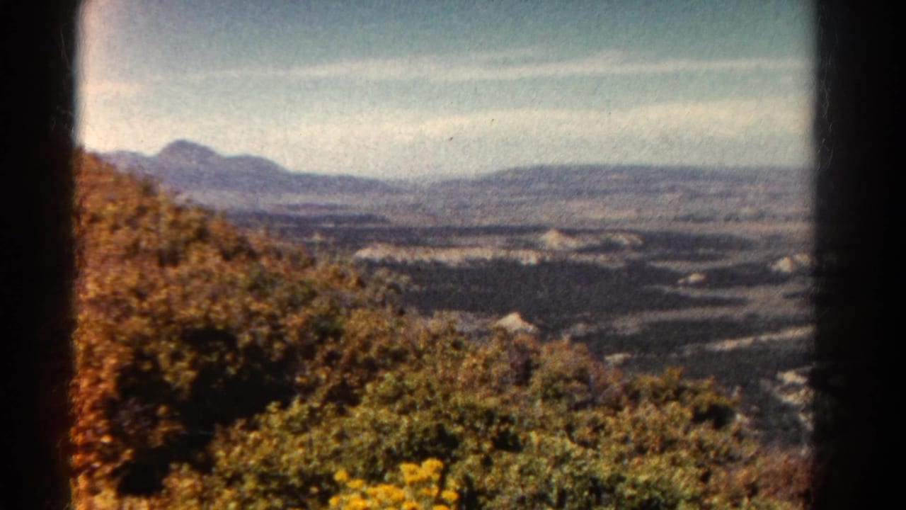 1967 Colorado home-movie frame from a high vantage point, with foreground brush, river bends, valley floor, and mountains beyond.