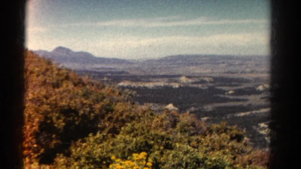 1967 Colorado home-movie frame from a high vantage point, with foreground brush, river bends, valley floor, and mountains beyond.