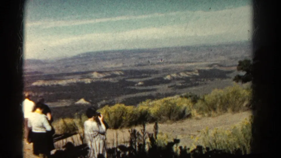 1967 Colorado travel frame showing a woman photographing the view from an overlook, with other visitors partly visible at left.