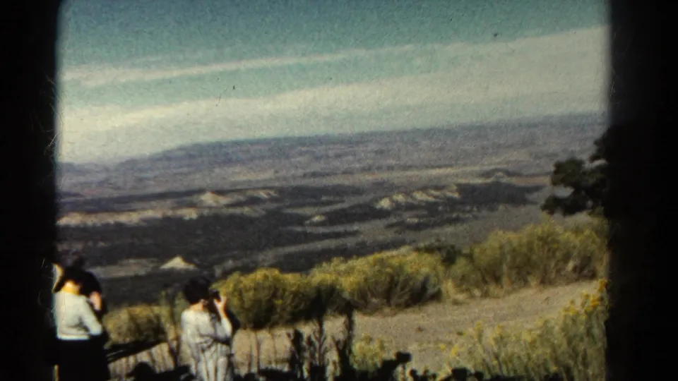 1967 Colorado home-movie frame with visitors near the overlook foreground and expansive hills and mesas beyond.
