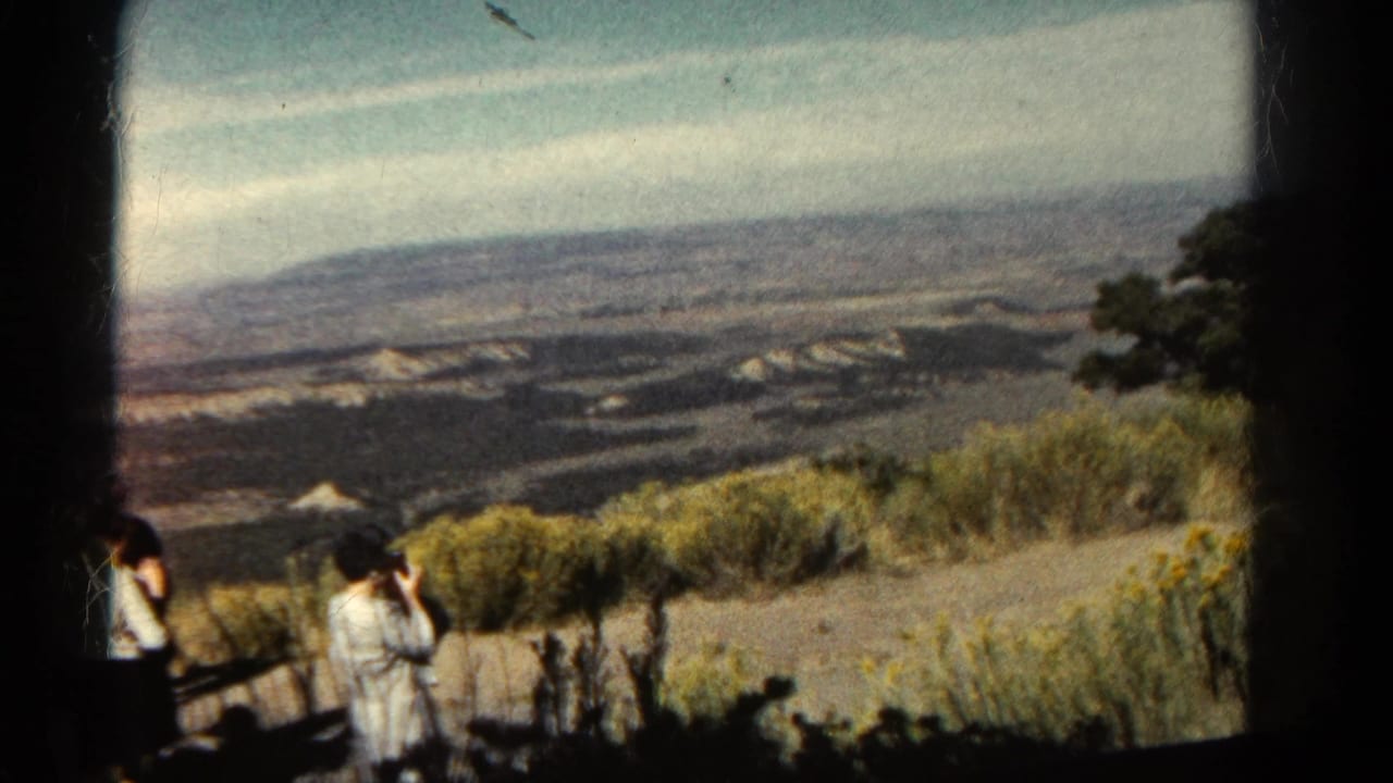 1967 Colorado 8mm frame of visitors at a canyon overlook, with a woman photographing the distant landscape.