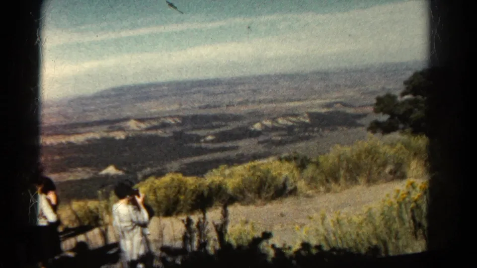 1967 Colorado 8mm frame of visitors at a canyon overlook, with a woman photographing the distant landscape.
