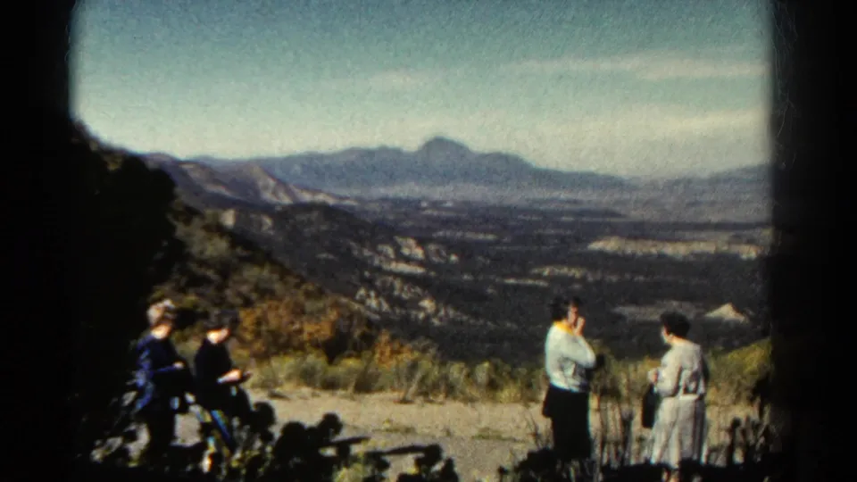 1967 Colorado 8mm frame of adults gathered at a canyon viewpoint, with distant mountains and scrub in view.