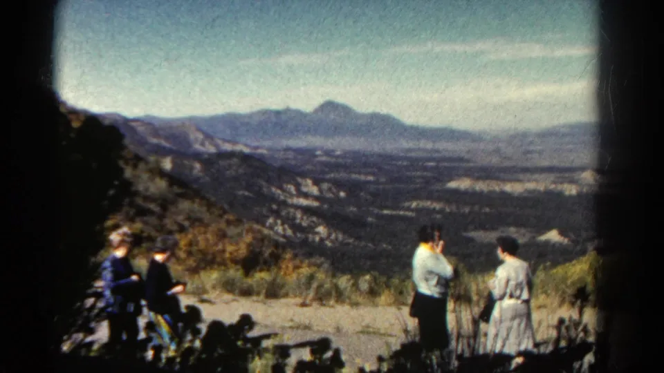 1967 Colorado home-movie frame of adults at a canyon viewpoint, including a woman in a light dress and distant mountain ridges.