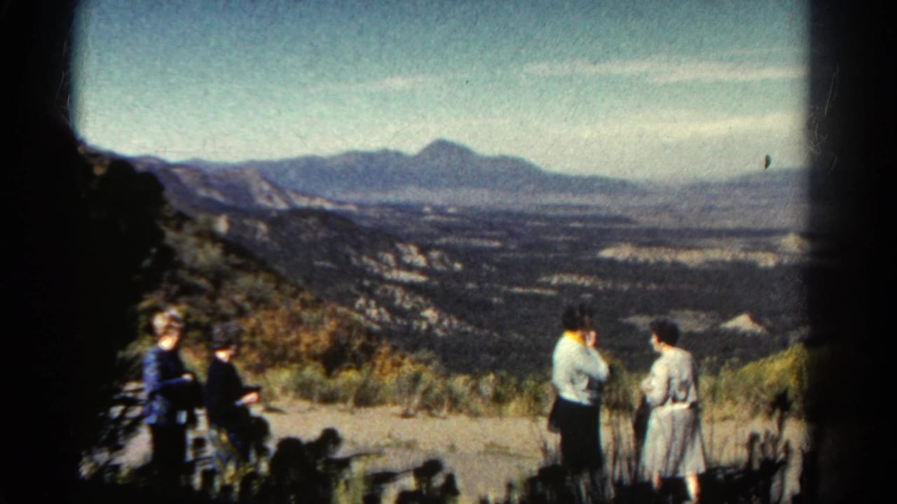 1967 Colorado home-movie frame showing three adult women at a mountain overlook, with one seated at left and two standing near the valley view.
