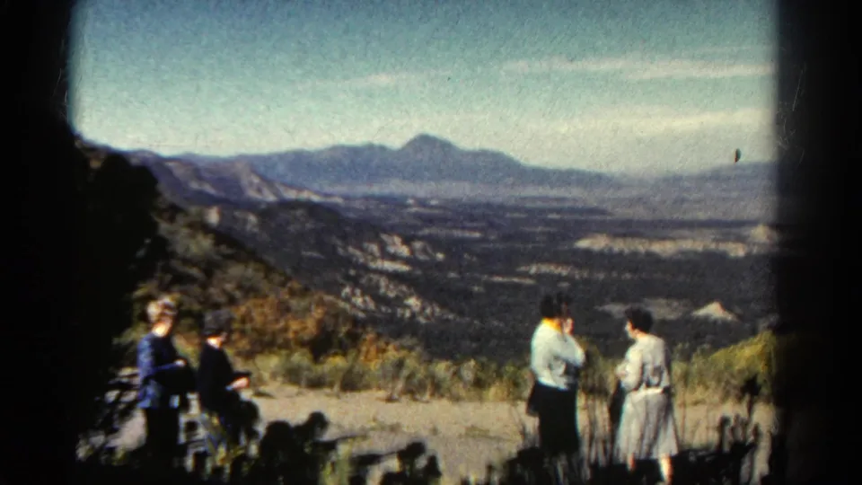 1967 Colorado home-movie frame showing three adult women at a mountain overlook, with one seated at left and two standing near the valley view.