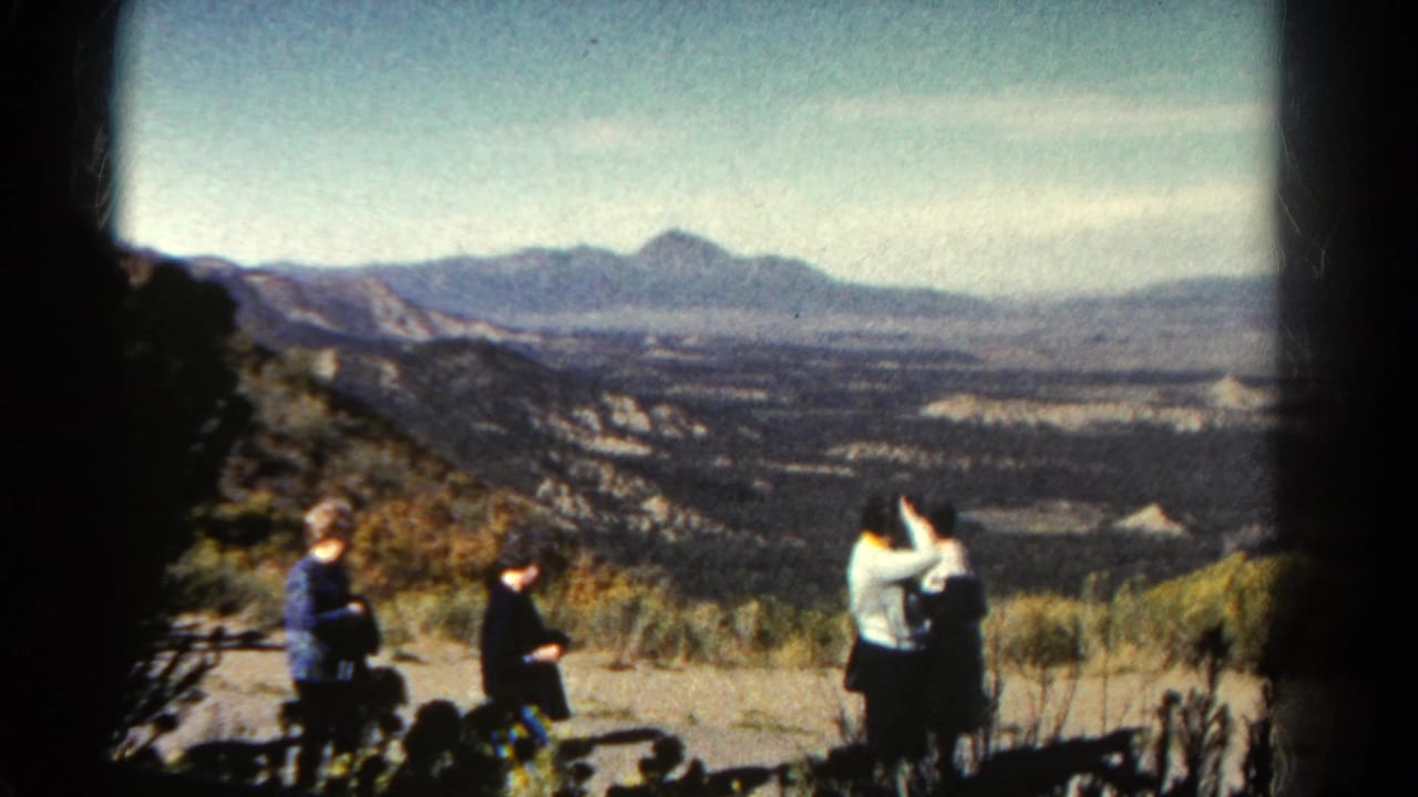 1967 Colorado home-movie frame showing people on a rocky overlook with distant valley and mountain ridges beyond.