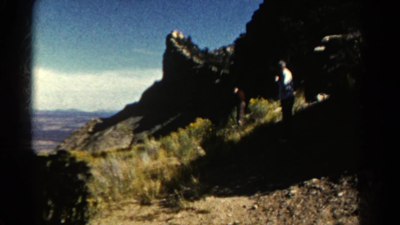 1967 Colorado 8mm frame with two small figures beside rugged rock, dry grasses, and a distant valley view.