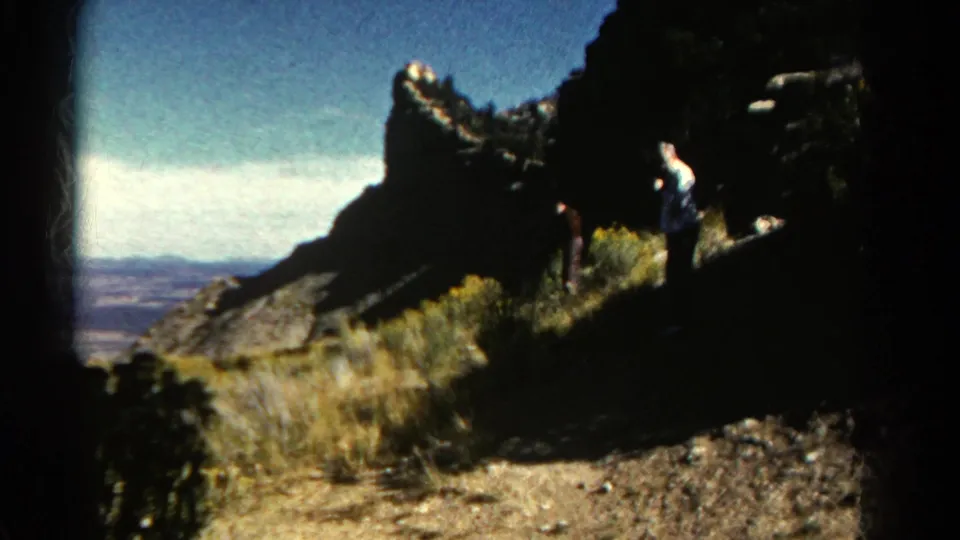 Colorado mountain home-movie frame from 1967 showing visitors near a rock face, dry grass, and distant landscape.