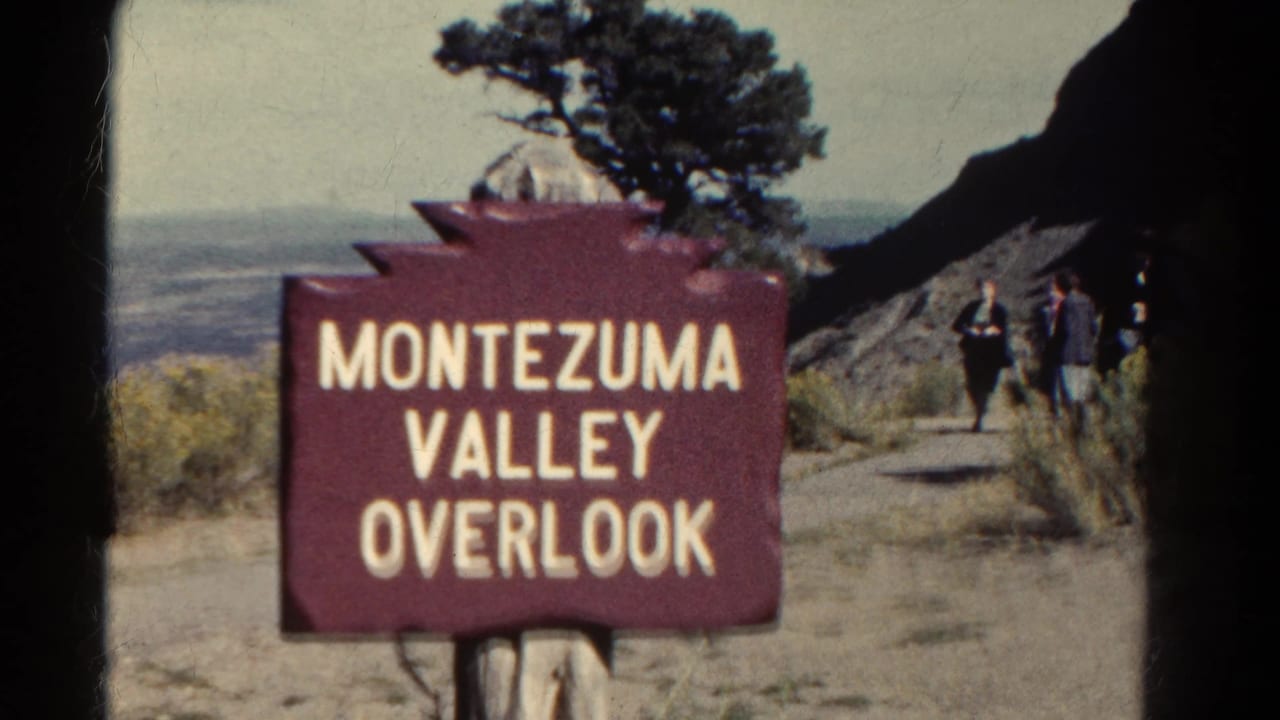 1967 8mm Colorado frame showing a red Montezuma Valley Overlook sign, distant valley, tree, and hikers on a path.