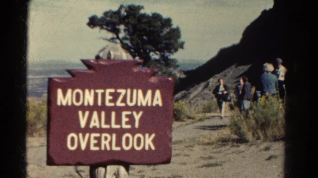 Maroon Montezuma Valley Overlook sign with tourists walking on a path near a rocky slope.