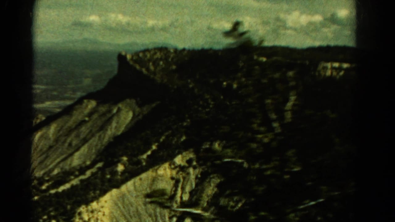 1967 Colorado 8mm view of a rugged cliff face and dark forested ridge, framed by heavy film-gate edges.