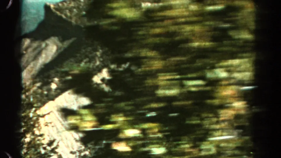 Blurred 1967 Colorado 8mm frame with a pale quarry face, passing trees, and dark cliff texture during a handheld pan or moving shot.
