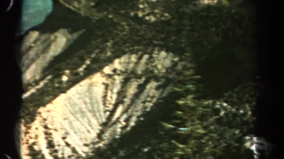 1967 Colorado 8mm frame showing a closer pale quarry cut below dark forested cliff layers, with heavy edge shadow from the film scan.