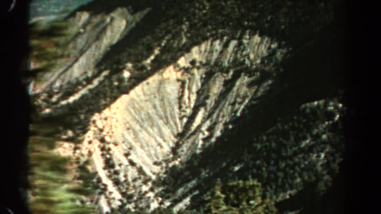 1967 Colorado 8mm frame showing a rugged rocky hillside with pale erosion lines and dense dark vegetation.