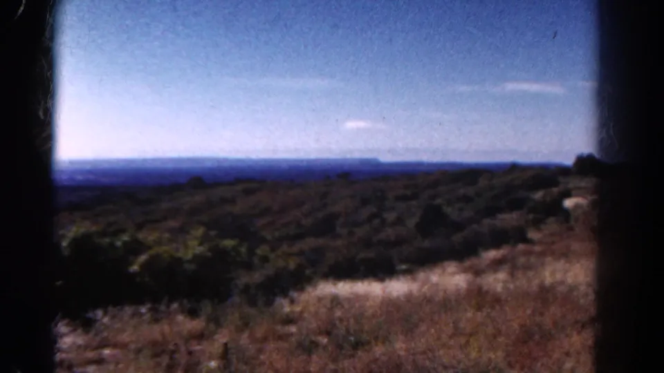 1967 Colorado 8mm view with dry foreground grasses, scattered brush, and a distant horizon line.