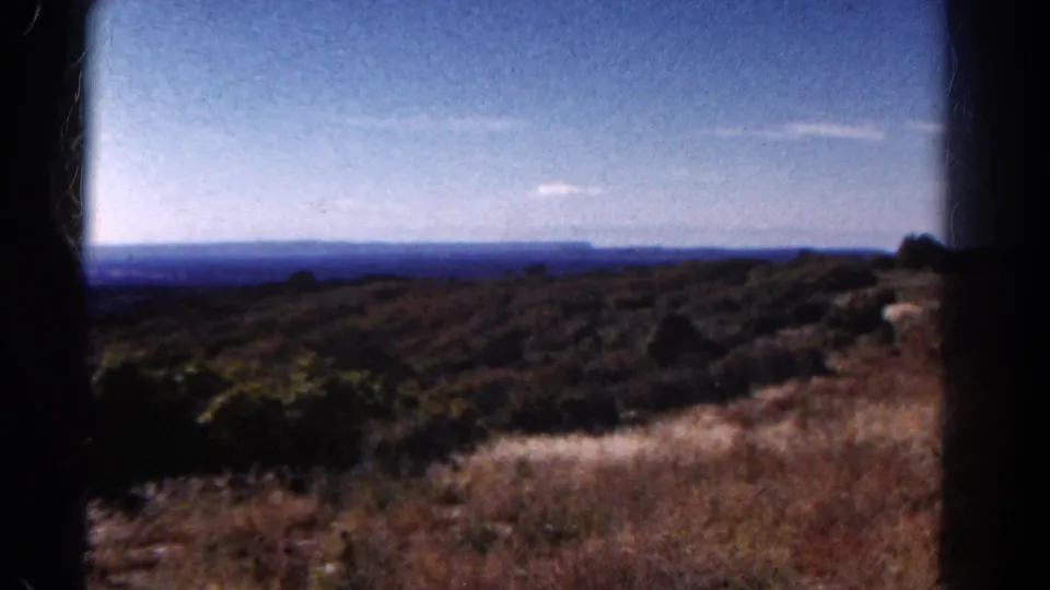 1967 Colorado home-movie frame showing brushy hillside, dry grassland, and a distant blue horizon.