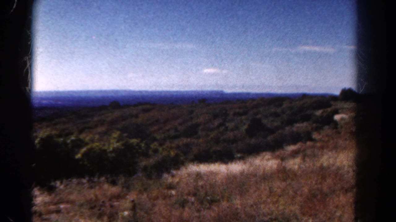 Brush-covered hills under blue sky with a distant horizon and black film borders.