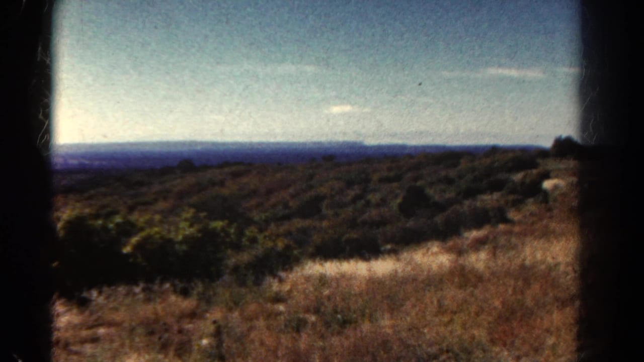 Open scrubland and distant hills beneath a pale blue sky, framed by film borders.