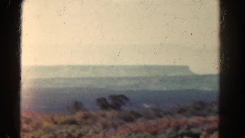 Soft 8mm Colorado landscape frame showing foreground brush, dry slope, and a hazy distant mesa or mountain form.