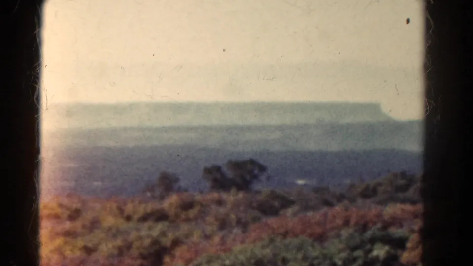 1967 Colorado 8mm frame showing a distant flat-topped landform, scrubby foreground vegetation, and soft film color.