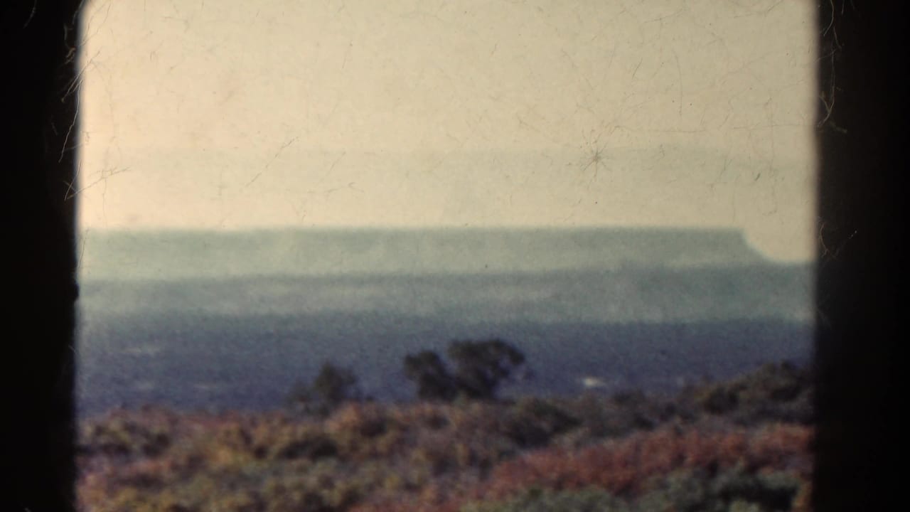 Hazy distant plateau above scrub brush, framed by dark 8mm film borders.