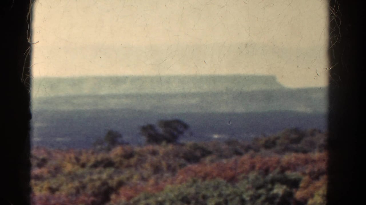 Distant flat-topped landform and muted brush seen through dark film gate edges.
