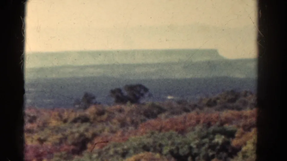1967 Colorado home-movie still showing low brush, a soft horizon, and a distant plateau partially obscured by haze.
